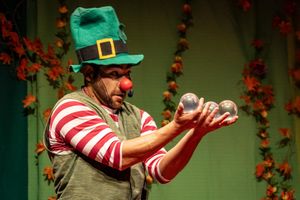 A person in a green leprechaun hat and red striped shirt performs a dance sequence against a dark floral background.