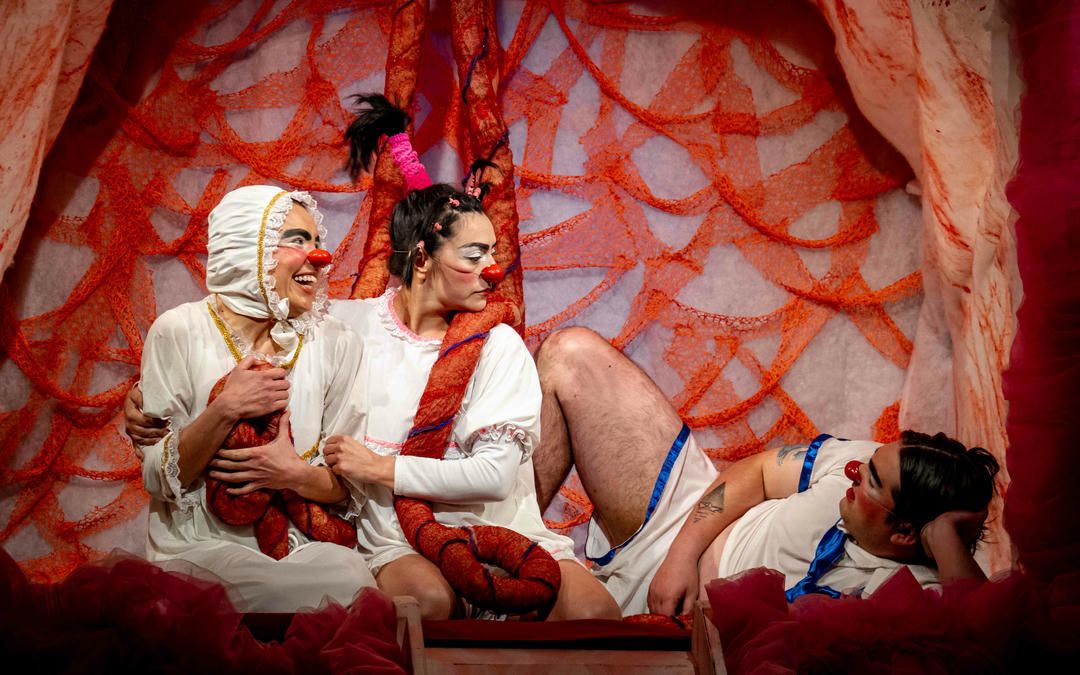 Dancers in red and white costumes perform an elegant ballet sequence against a textured red backdrop.