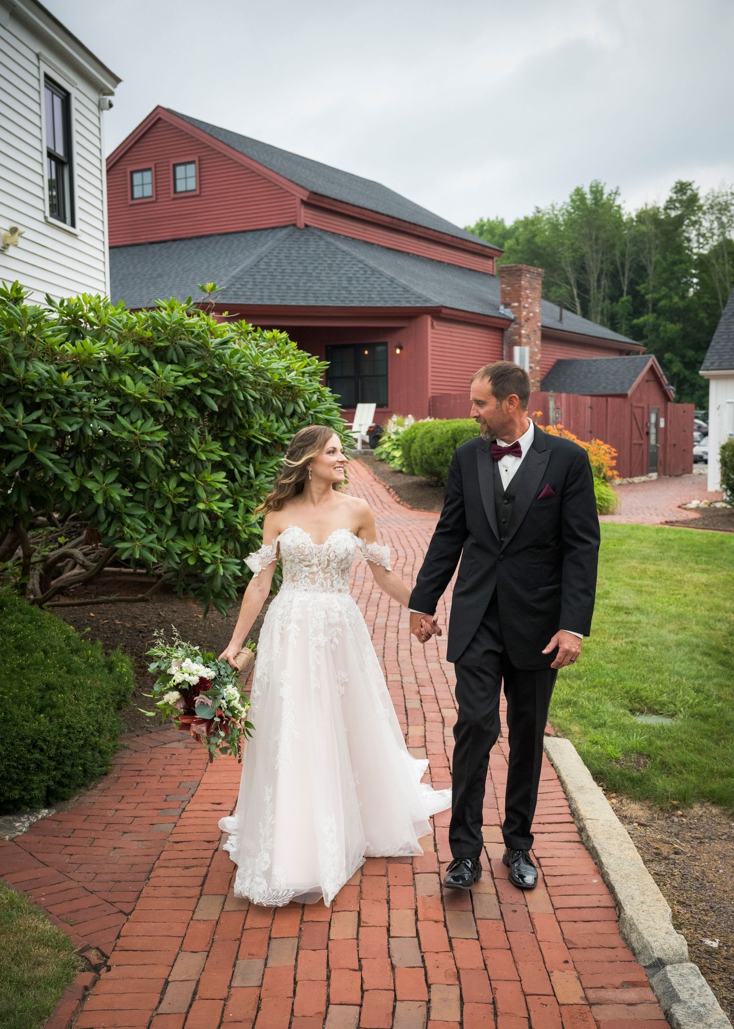 A couple shares a romantic moment on a grassy hill with red barn buildings in the background.