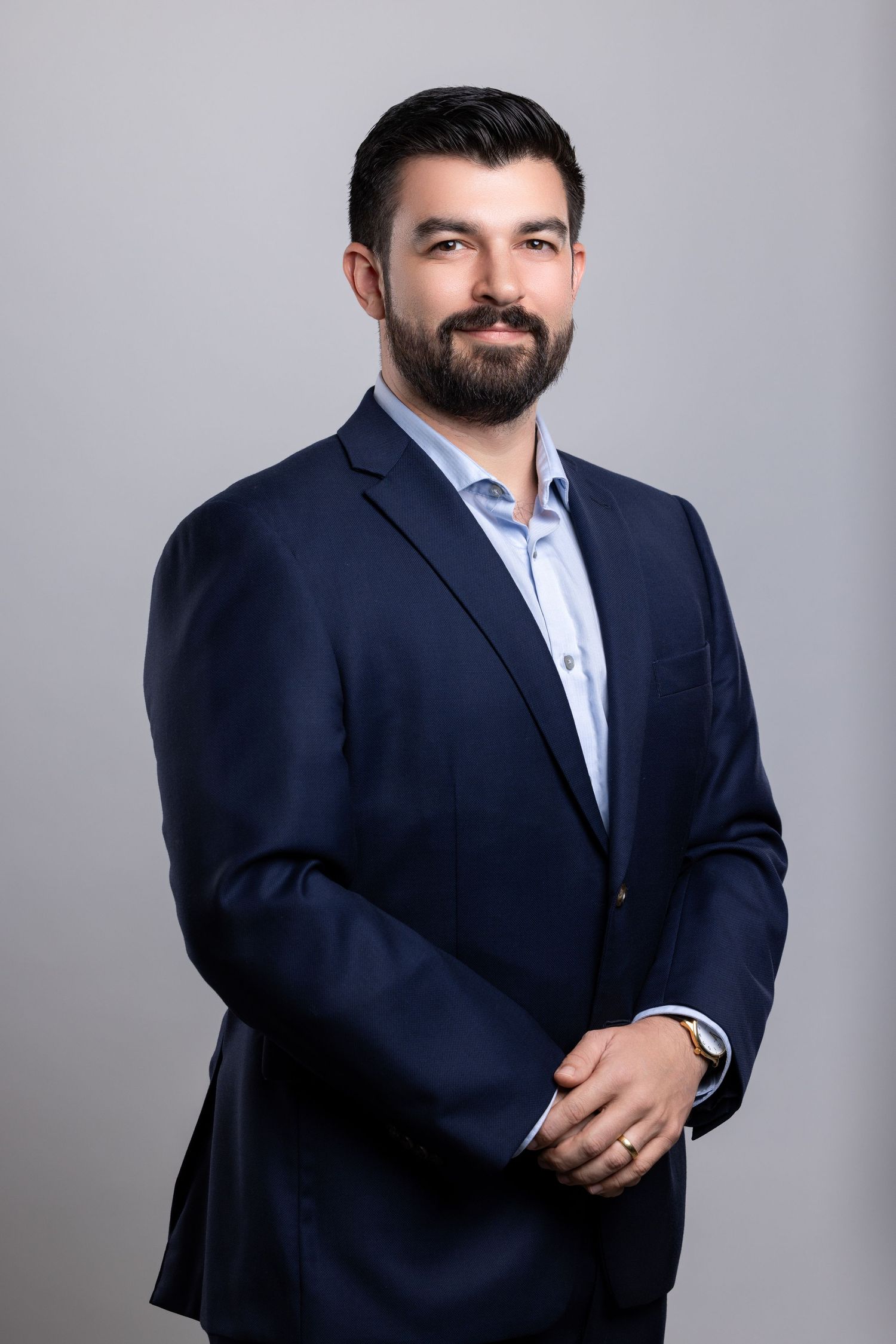 Professional headshot of a person in a navy suit and light blue dress shirt against a gray background.