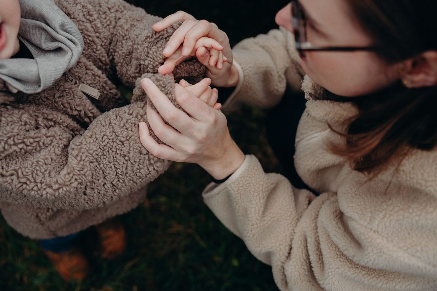 Mother gently holds her toddlers tiny hands in a close-up outdoor portrait.