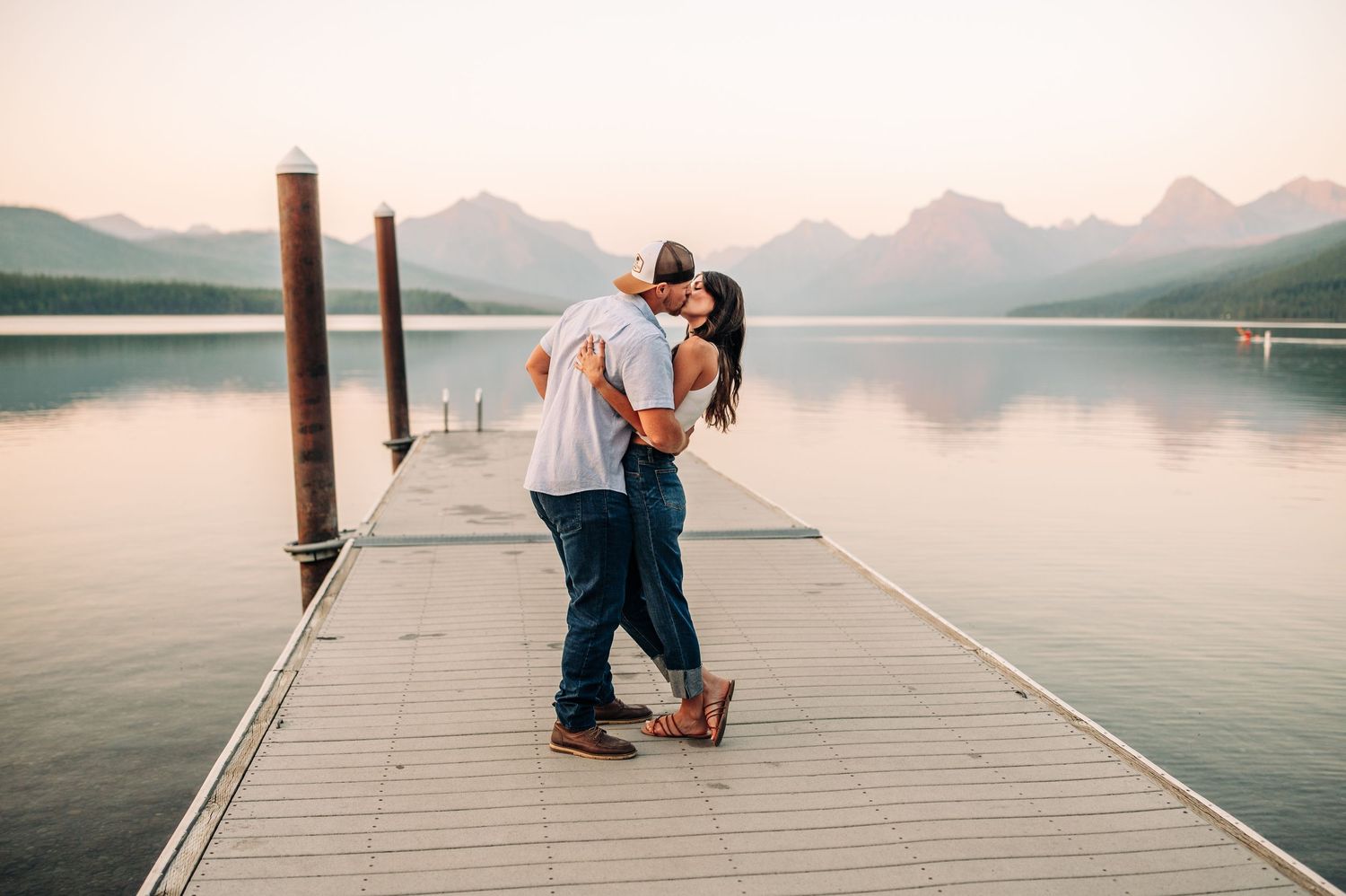 Romantic couple embraces on wooden dock overlooking tranquil mountain lake at sunset.