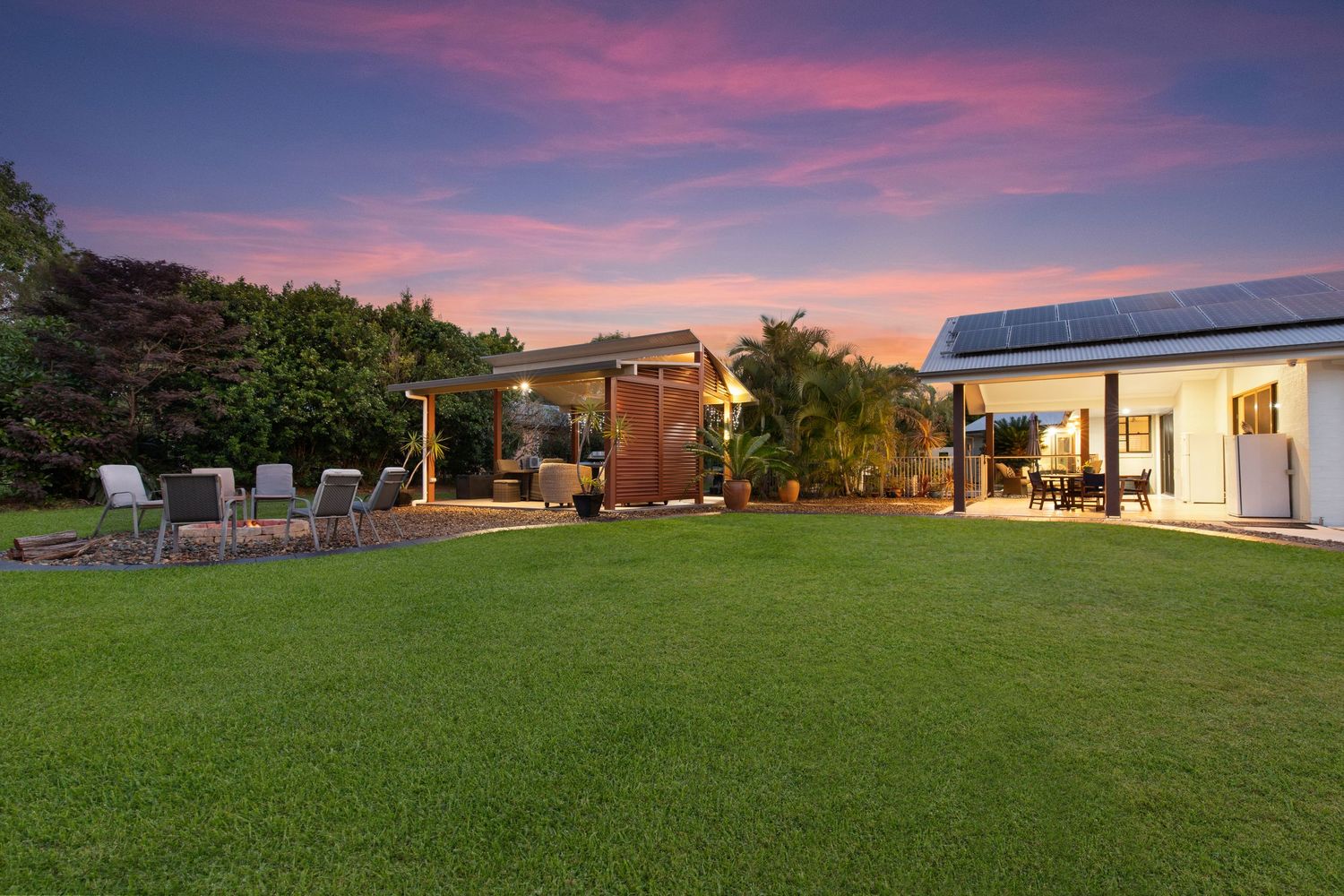 Spacious backyard with manicured lawn, solar panels, and outdoor entertaining area at sunset.