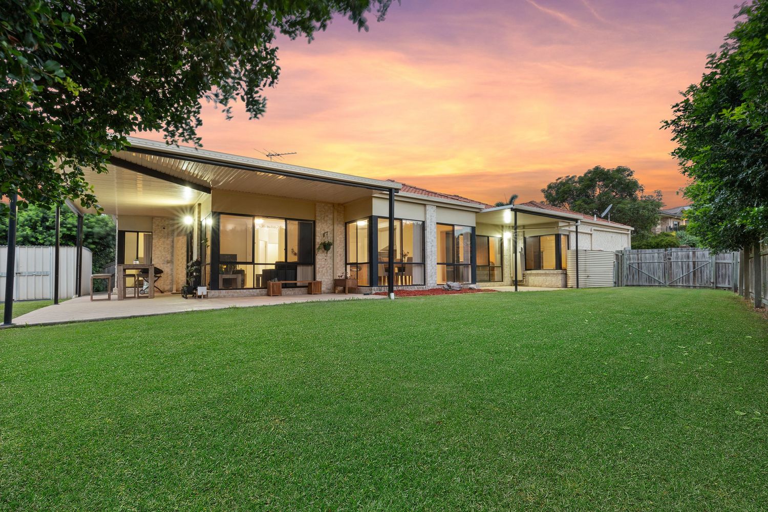 Modern single-story home with expansive glass facade and large lawn at sunset.