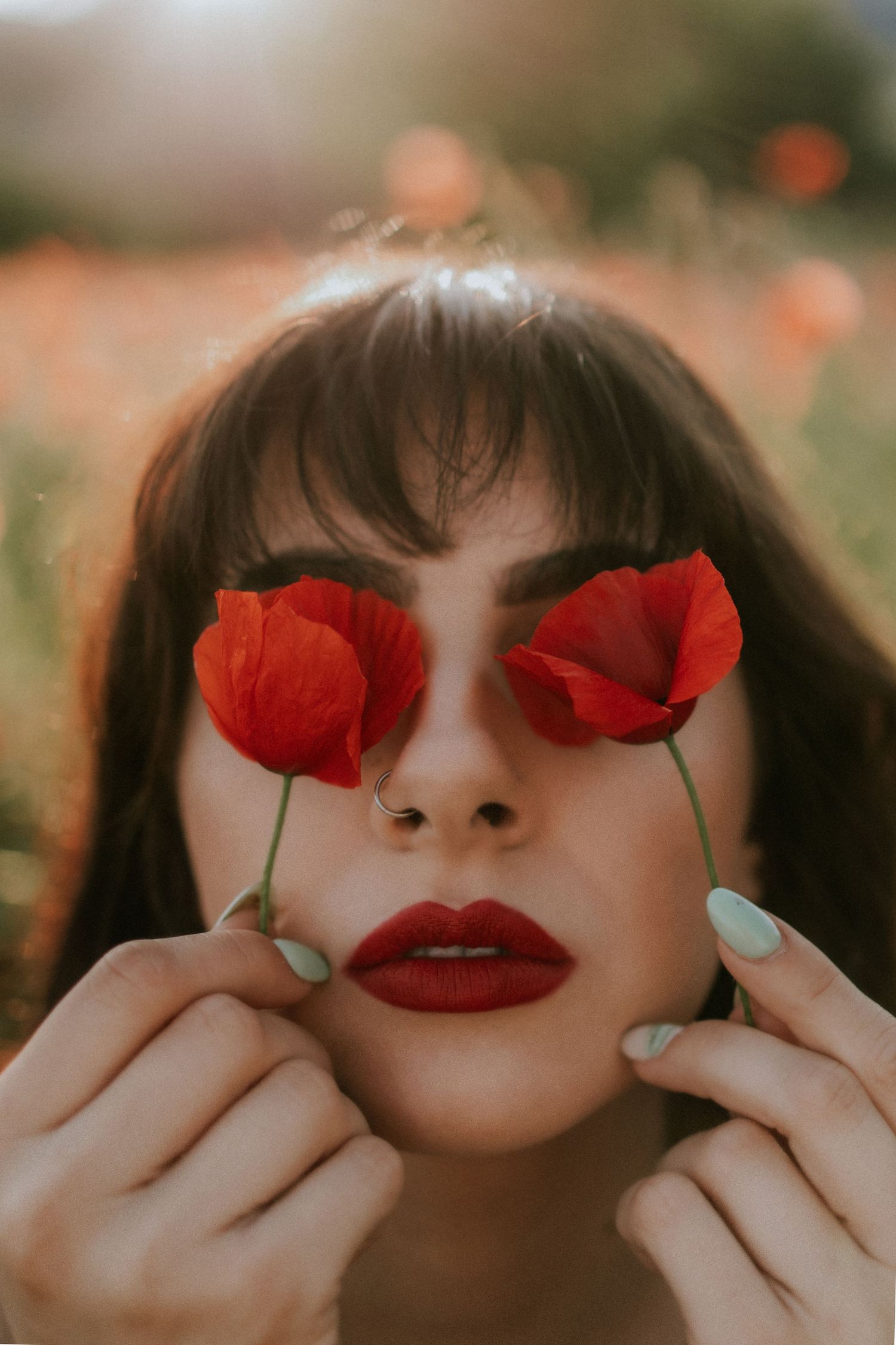Detailný portrét ženy s červeným rúžom, ktorá si zakrýva oči dvoma červenými makmi v poli. Umelecká fotografia, Rajecké Teplice.