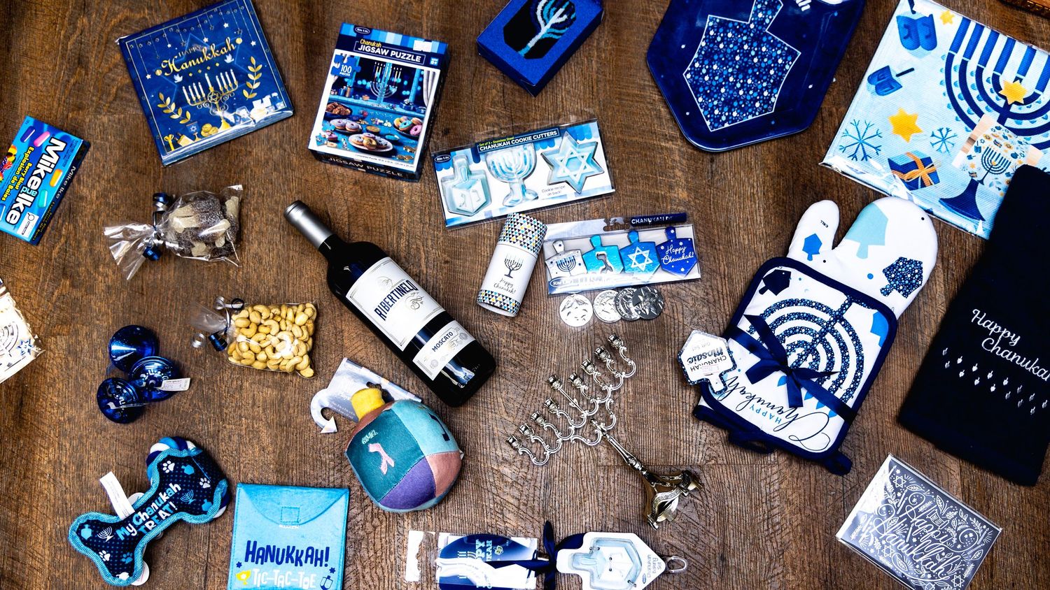 Various blue and white Hanukkah-themed decorations, cards, and gifts scattered on a rustic wooden table surface.