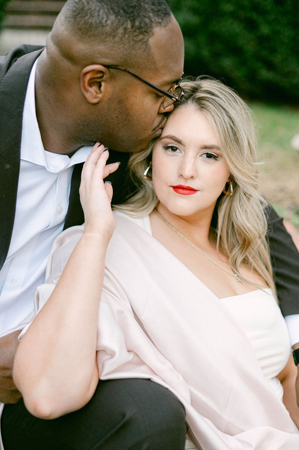 A romantic couple shares an intimate moment outdoors in formal attire.