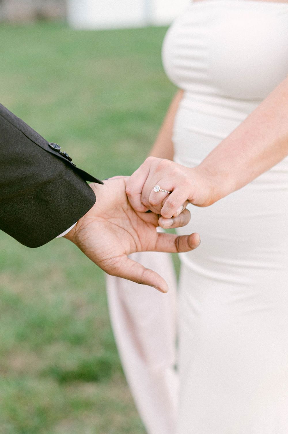 Close-up view of hands exchanging wedding rings during an outdoor ceremony on a grassy lawn.