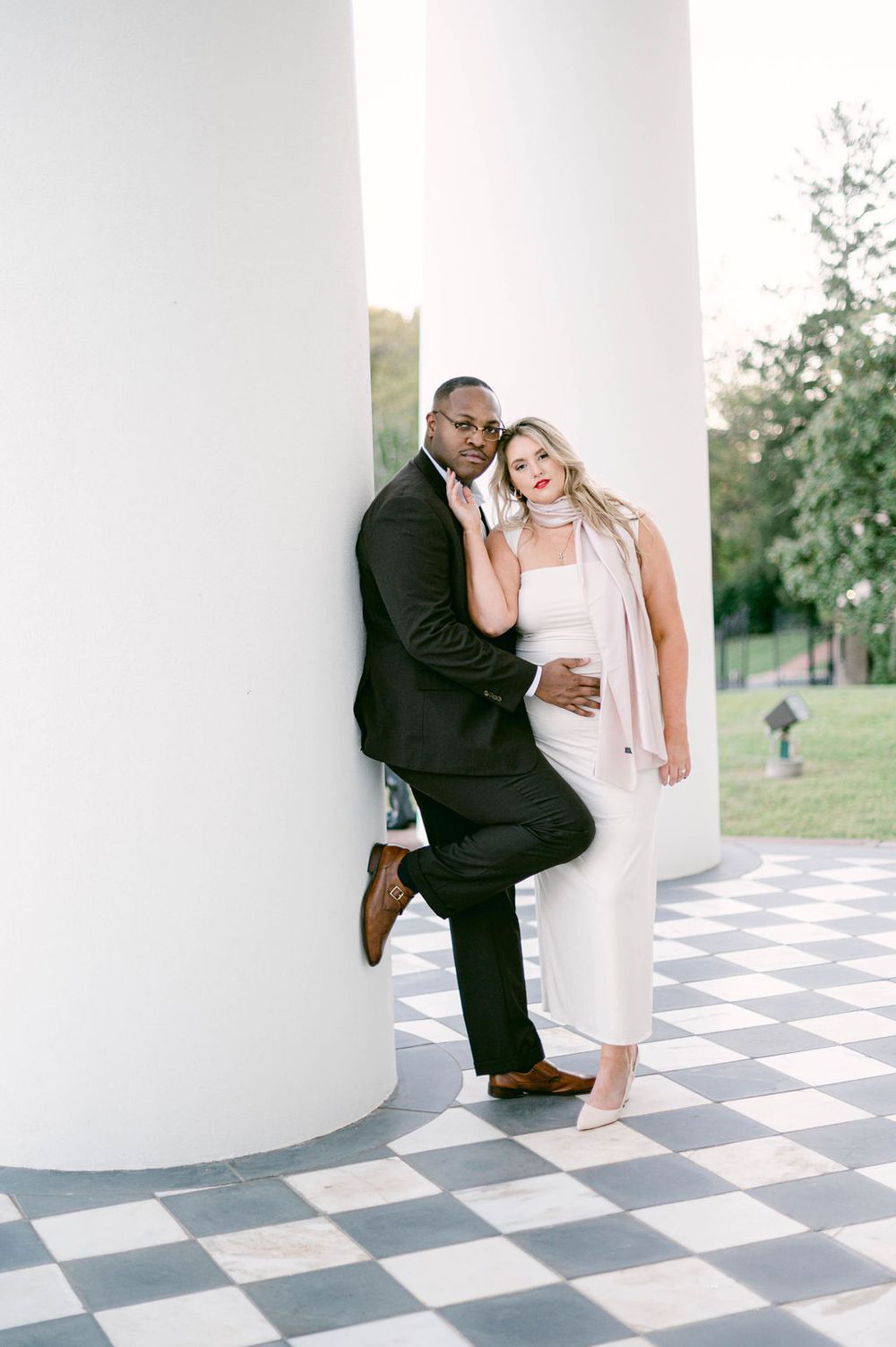 A couple shares a playful moment on a black and white checkered floor in an outdoor pavilion setting.