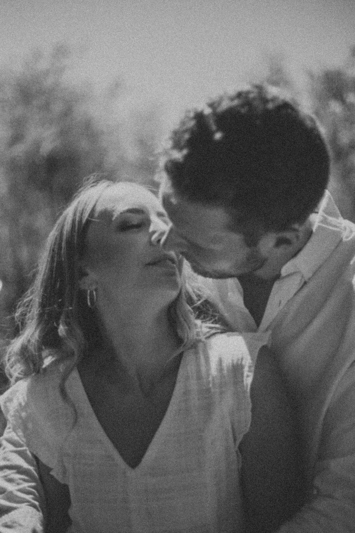 Black and white close-up of a couple sharing a tender kiss outdoors in a natural setting.