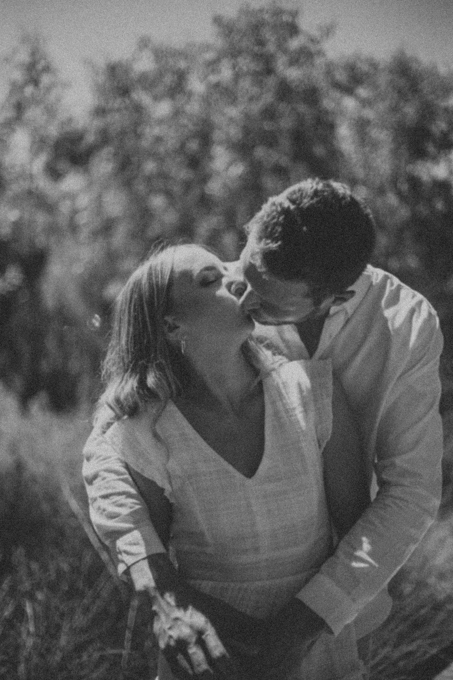 Black and white romantic photo of a couple kissing passionately in an outdoor natural landscape.