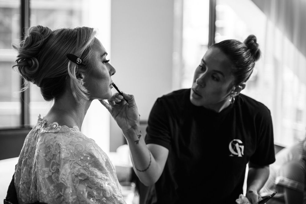 Black and white photo showing makeup application during wedding preparations.