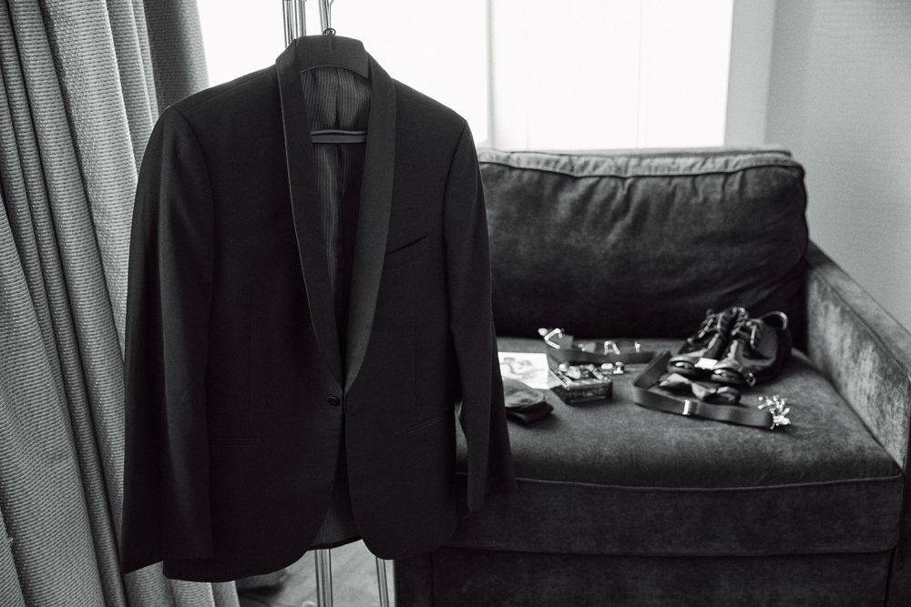 A black blazer hangs next to a dark couch with scattered items in a monochrome interior setting.
