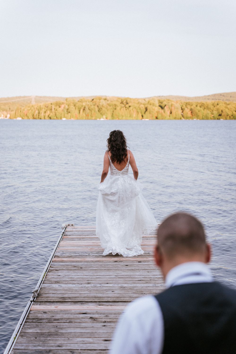 Un couple partage un moment romantique sur un quai en bois face à un lac paisible, au coucher du soleil d’automne.