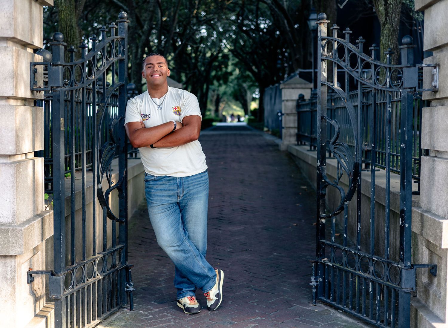 Person sitting on stone steps by ornate iron gates in a dimly lit passageway.