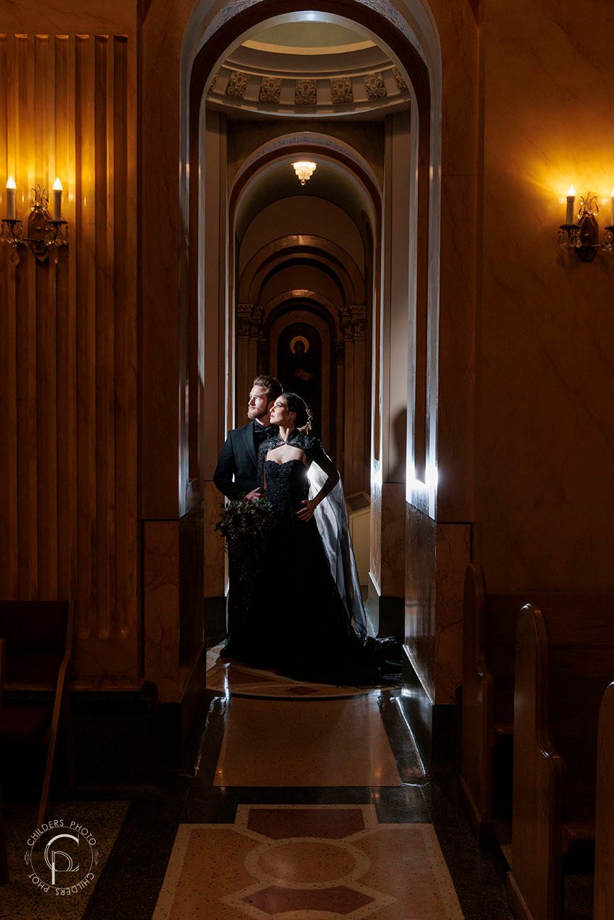 Couple stands in dramatic arched hallway with warm lighting and elegant architectural details at night. Dayton Ohio Greek Church wedding.