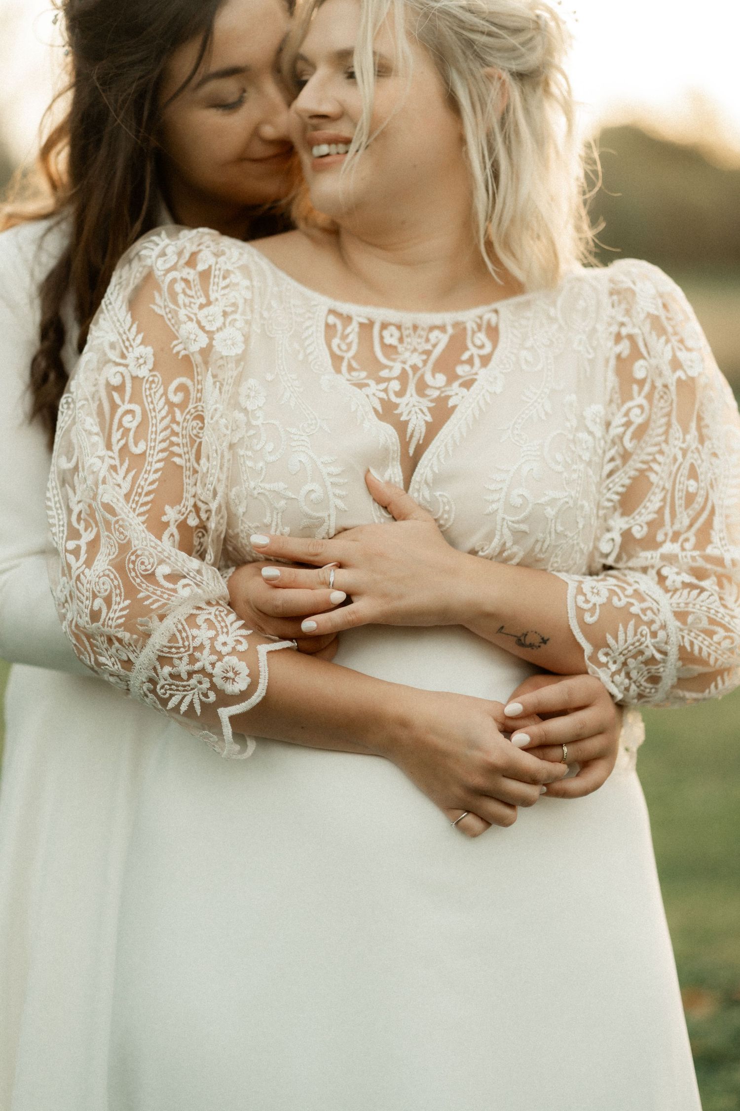 Close-up details of delicate white lace on a wedding dress with intricate floral embroidery patterns in warm sunlight.