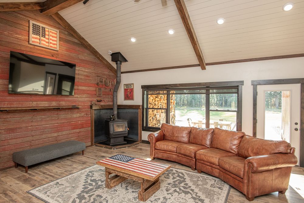 Modern living room features exposed wood beams, brown leather sectional sofa, and geometric area rug on hardwood floors.