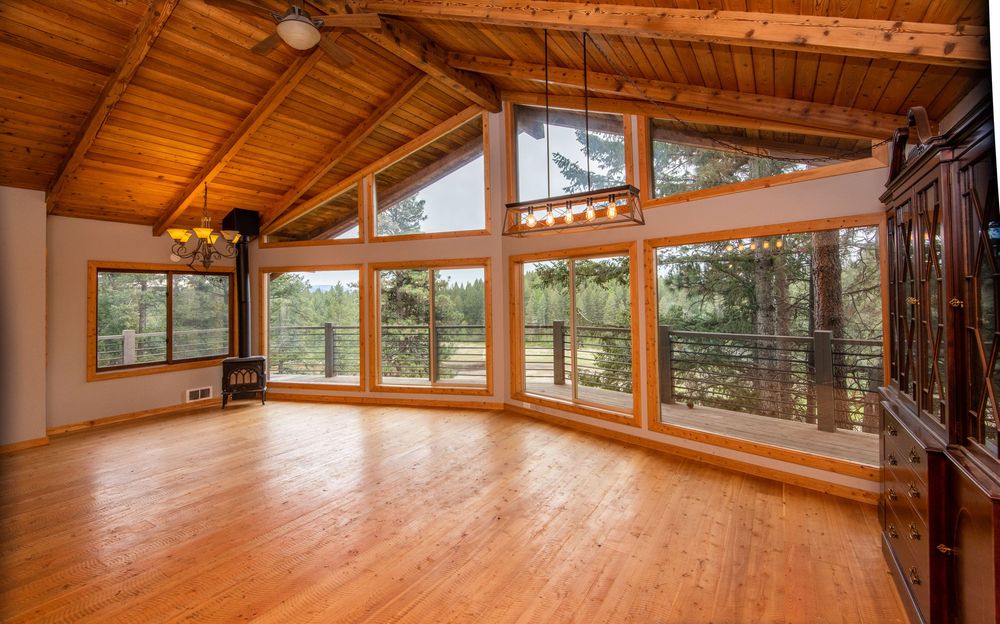 Large wooden dance studio with polished hardwood floors, exposed beams, and panoramic windows offering natural light.