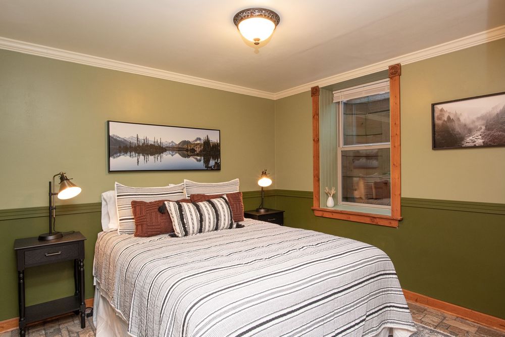 Cozy bedroom interior with green walls, wooden trim, and white bedding in a rustic mountain lodge setting.