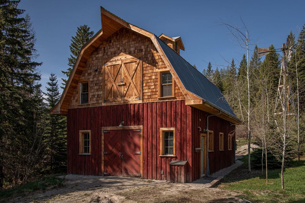 Row of red barn-style cabins nestled among evergreen trees against a bright blue mountain sky.