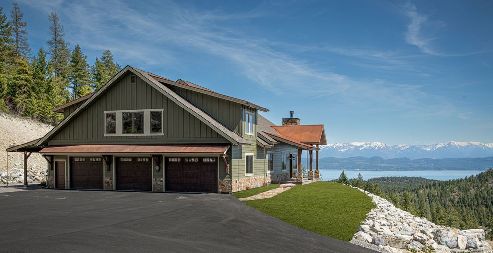 A panoramic view of modern mountain homes nestled among evergreen trees with blue skies and distant peaks in the background.