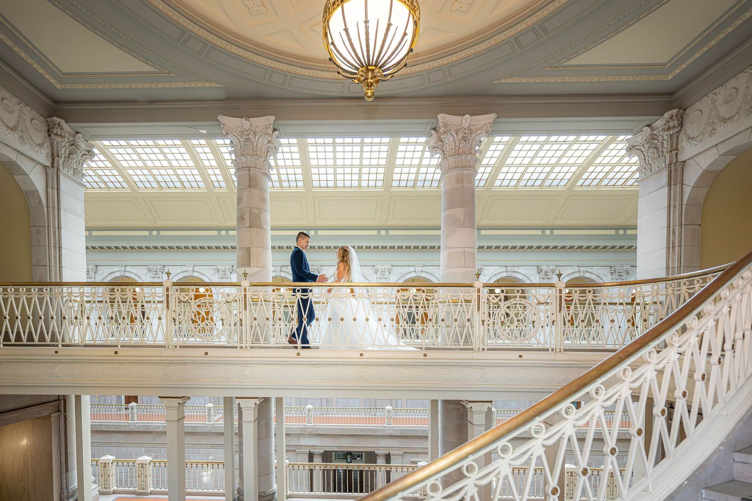 Elegant white marble staircase and balcony in a grand historic building with ornate architectural details and chandelier.
