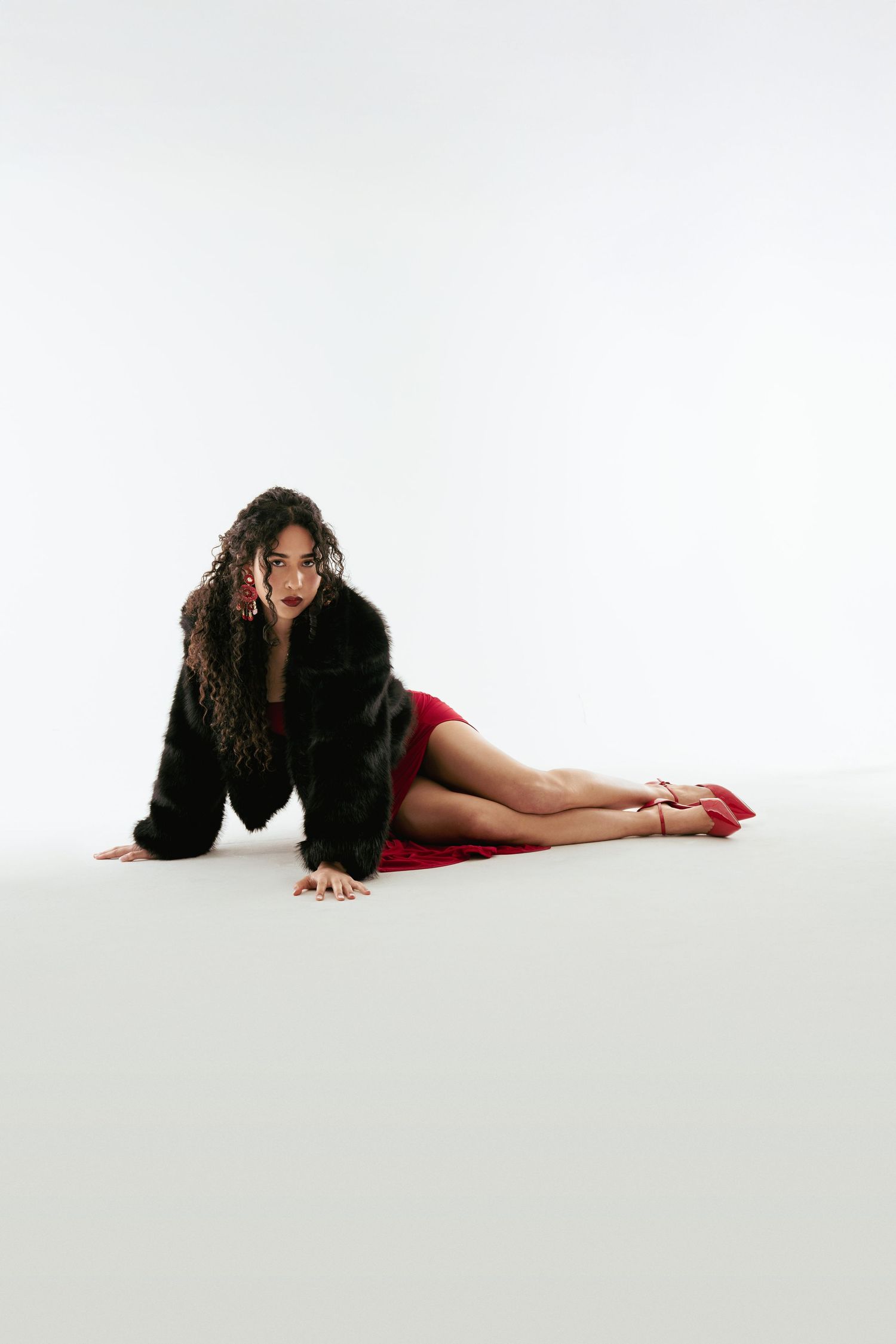 A person in black and red attire performs a dramatic floor pose sequence against a white backdrop.