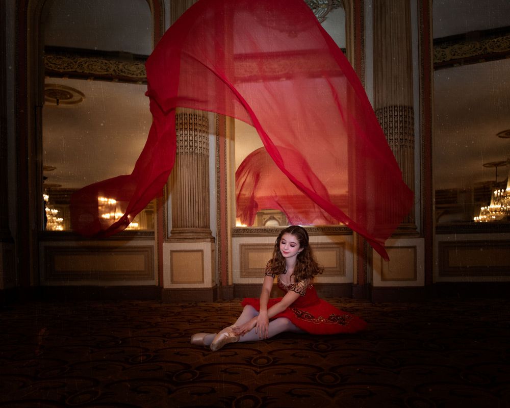 Artistic dance photo featuring flowing red fabric in elegant ballroom with chandeliers.