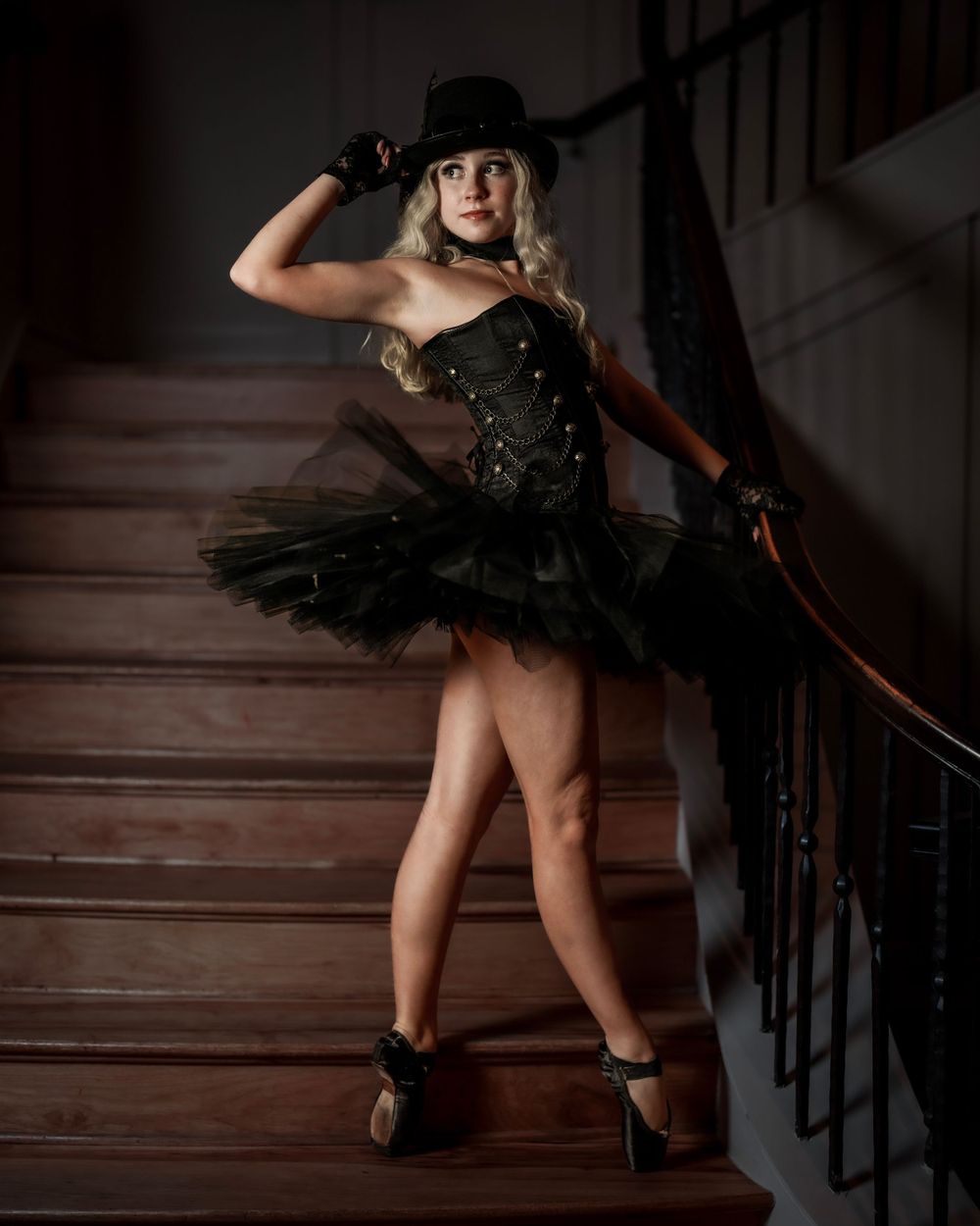 Dancer strikes dramatic pose on staircase wearing black tutu and steampunk-inspired costume.