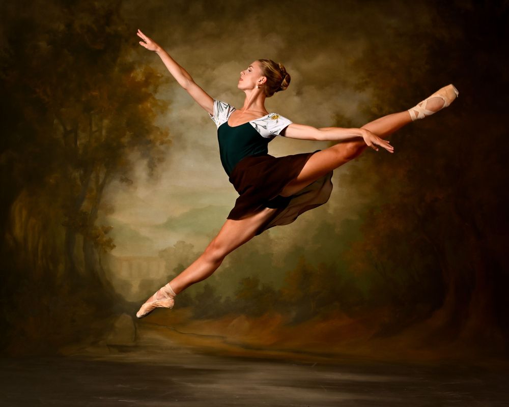 Dancer leaps gracefully through the air in a dramatic split pose against a dark backdrop.