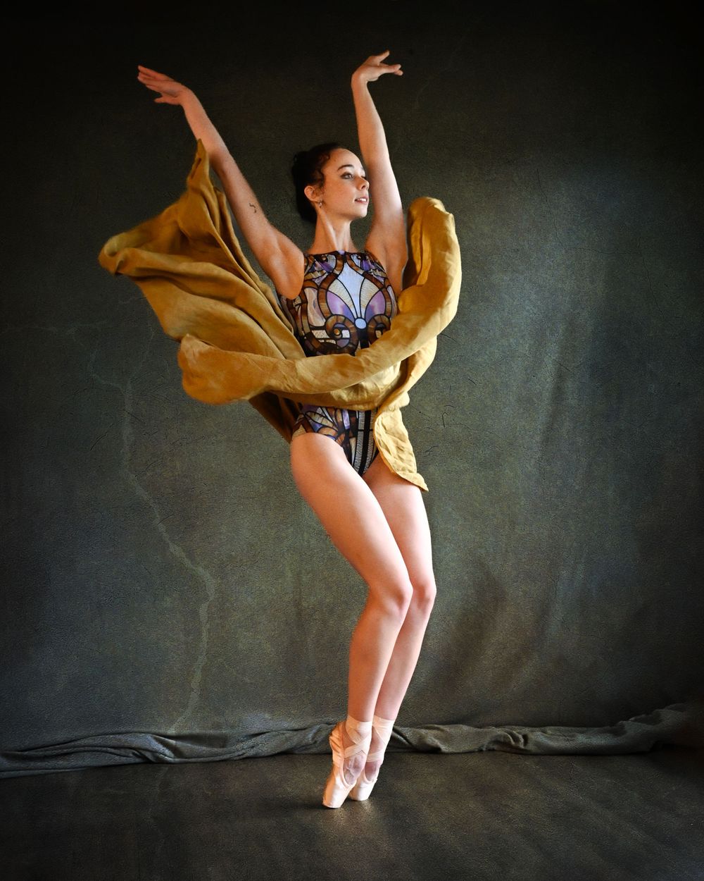 Dancer in yellow flowing skirt and patterned leotard performs elegant pose on pointe.