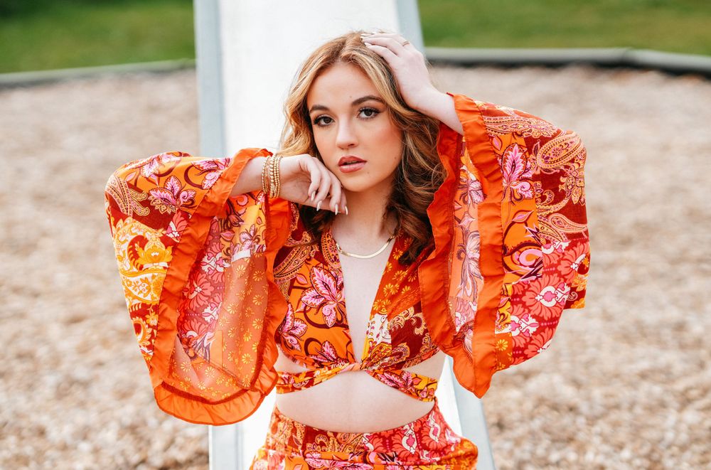 A vibrant orange floral dress with dramatic bell sleeves photographed in an outdoor setting.