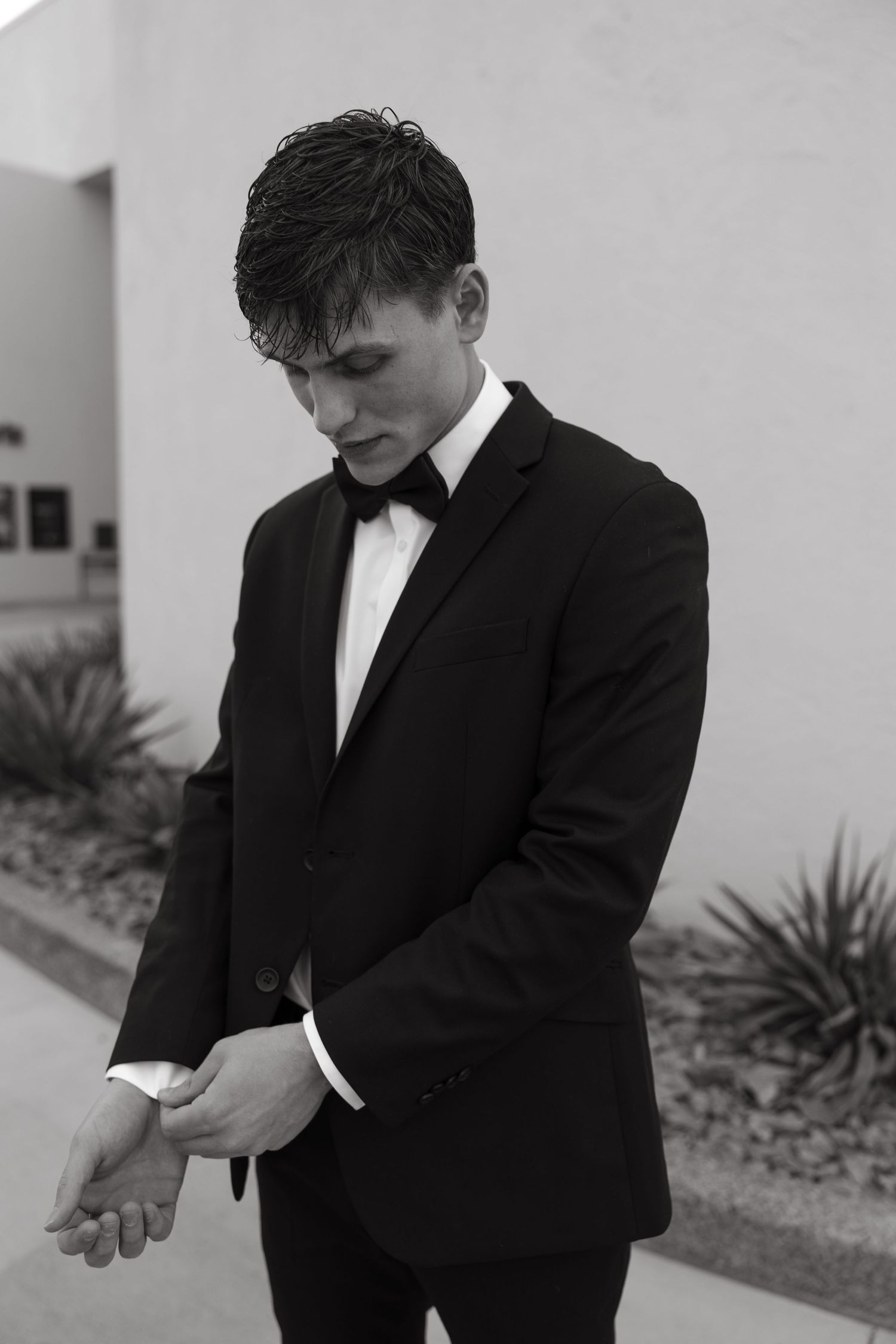 Black and white portrait of groom adjusting cufflinks in formal attire.
