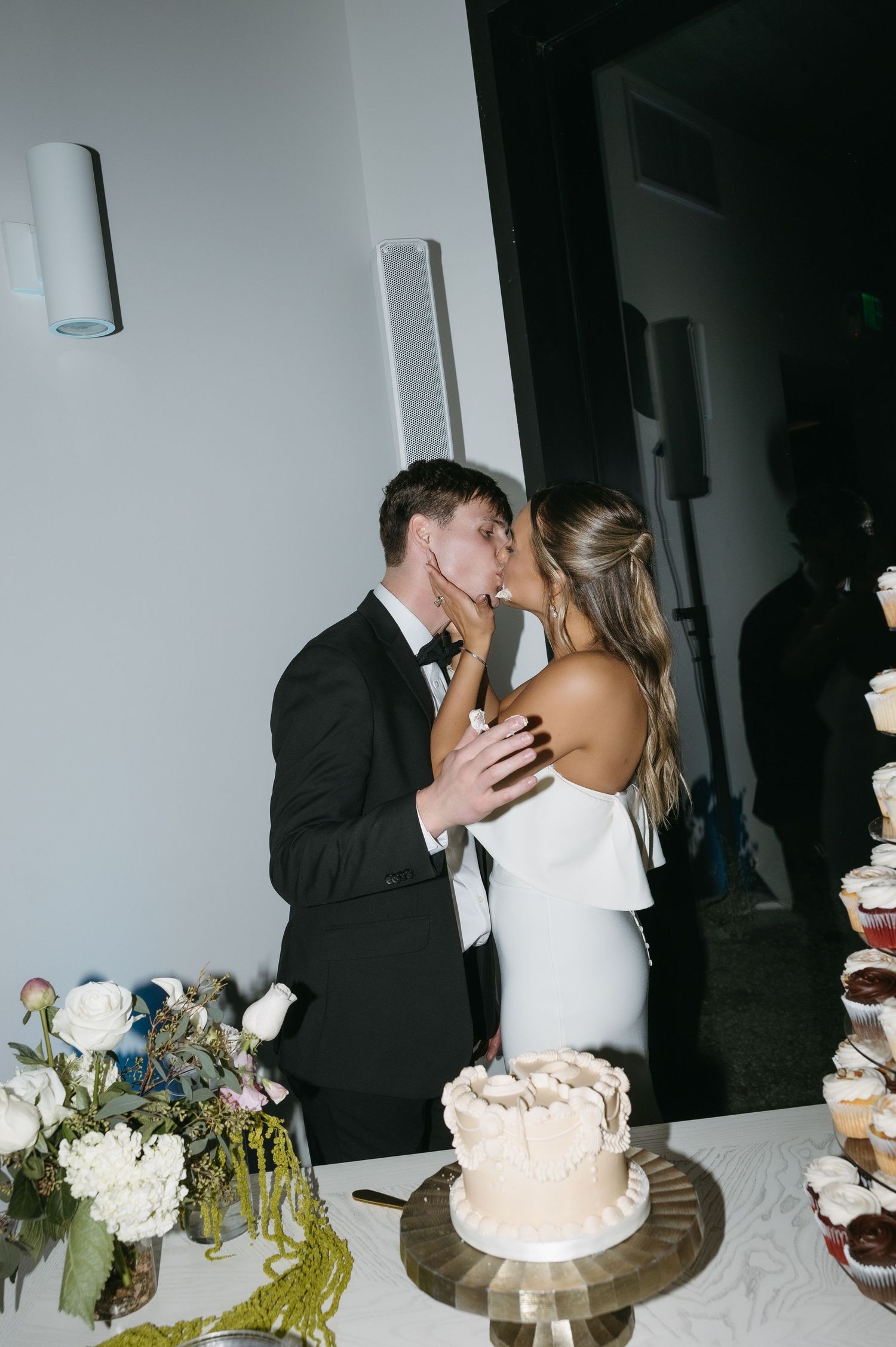 A couple kisses next to their wedding cake during the reception.