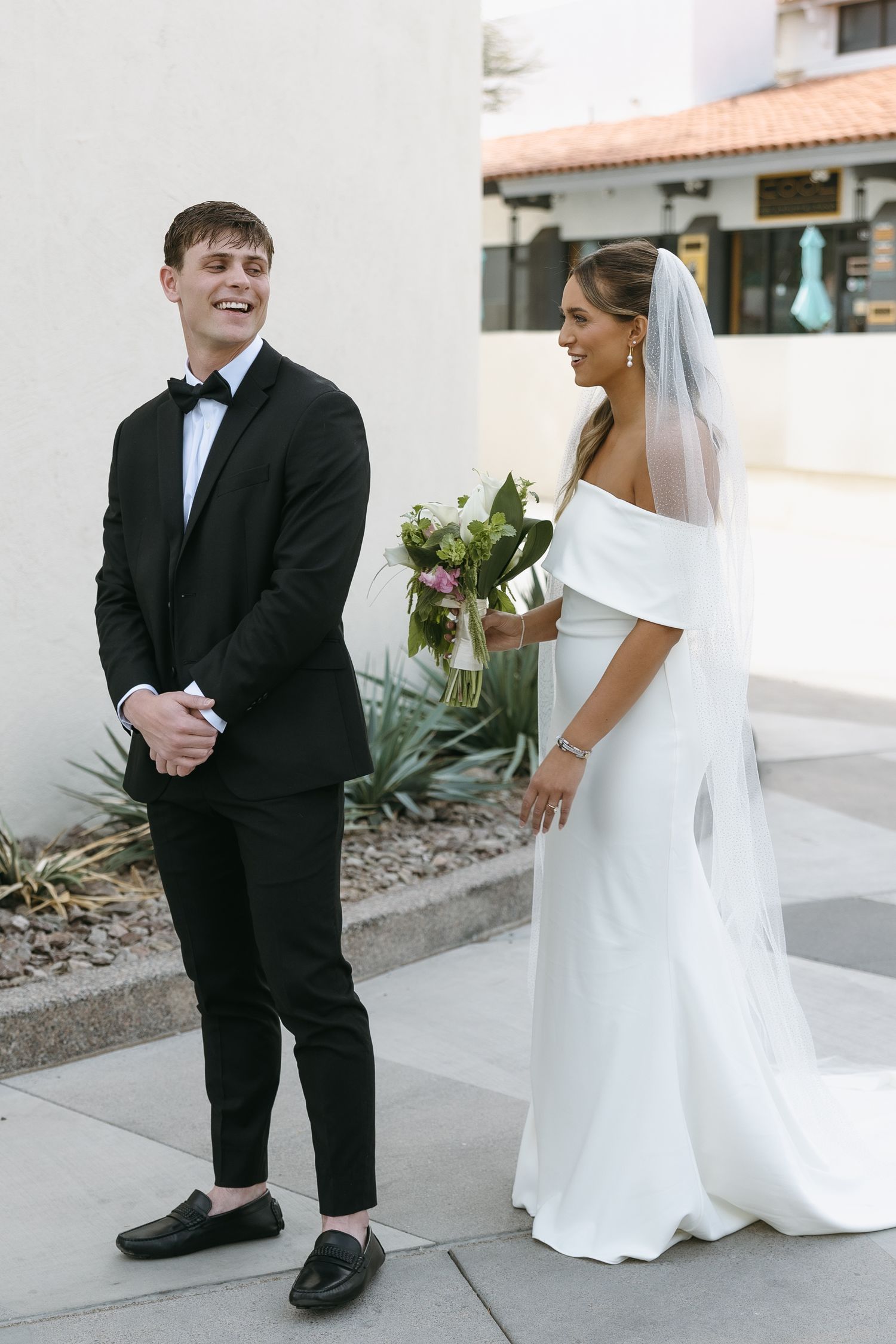 First look wedding moment between couple in elegant attire against white wall.