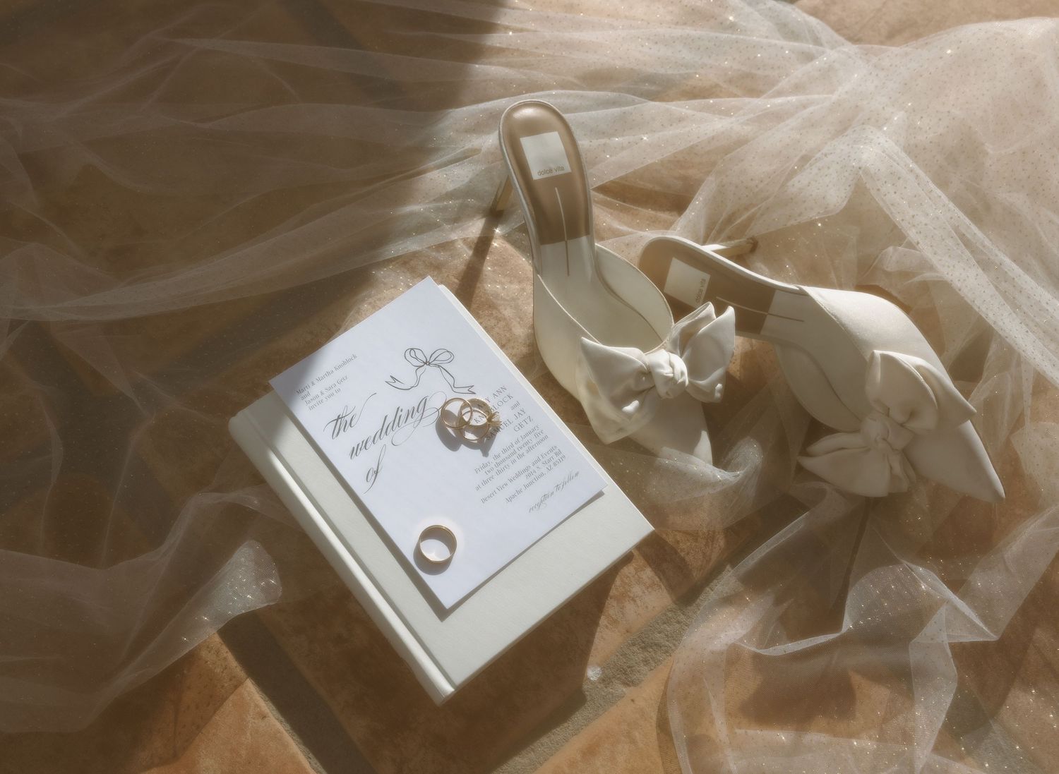 Wedding invitation and rings styled with delicate tulle fabric in soft lighting.
