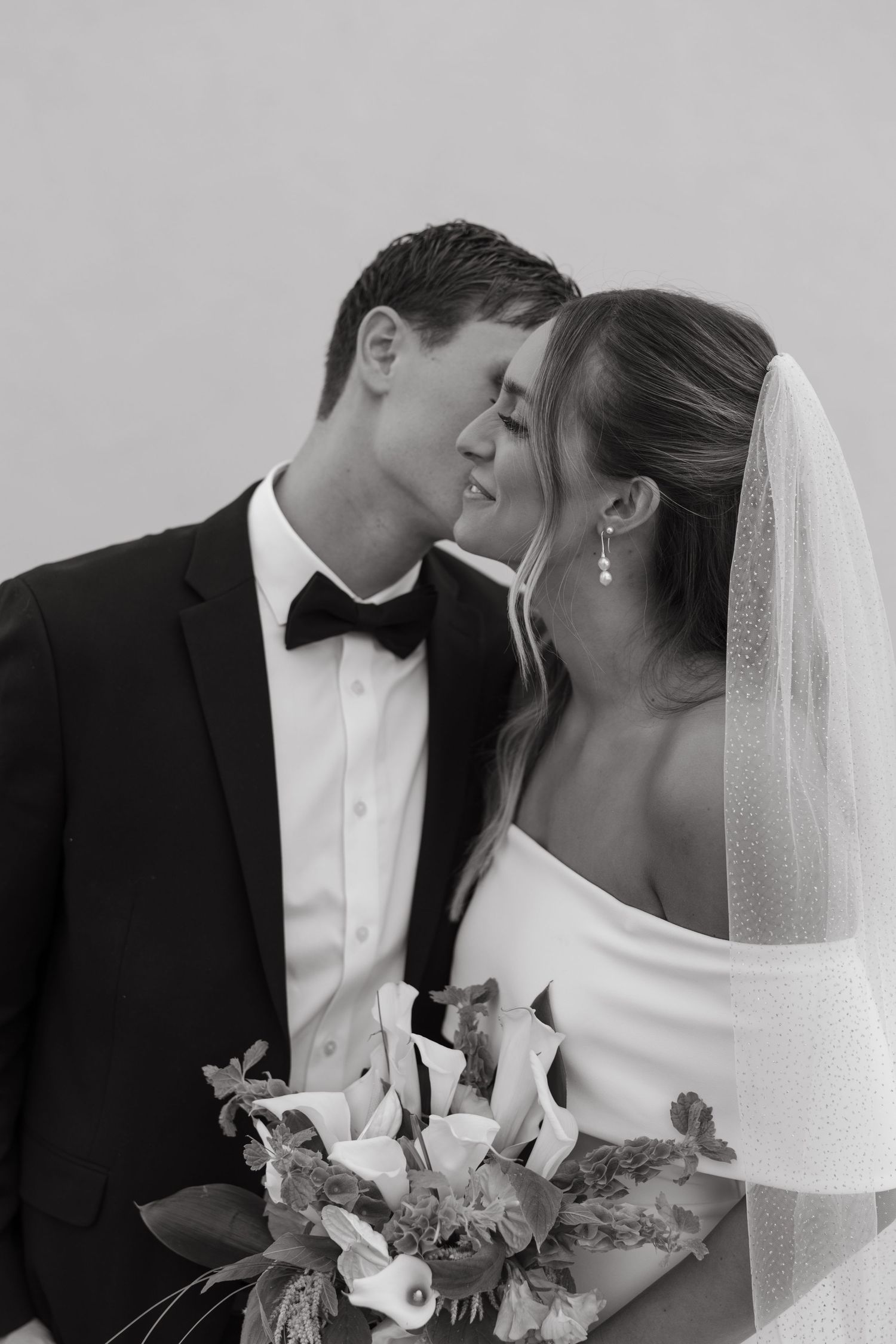 Black and white romantic wedding photo showing couple sharing intimate moment with bride holding floral bouquet.
