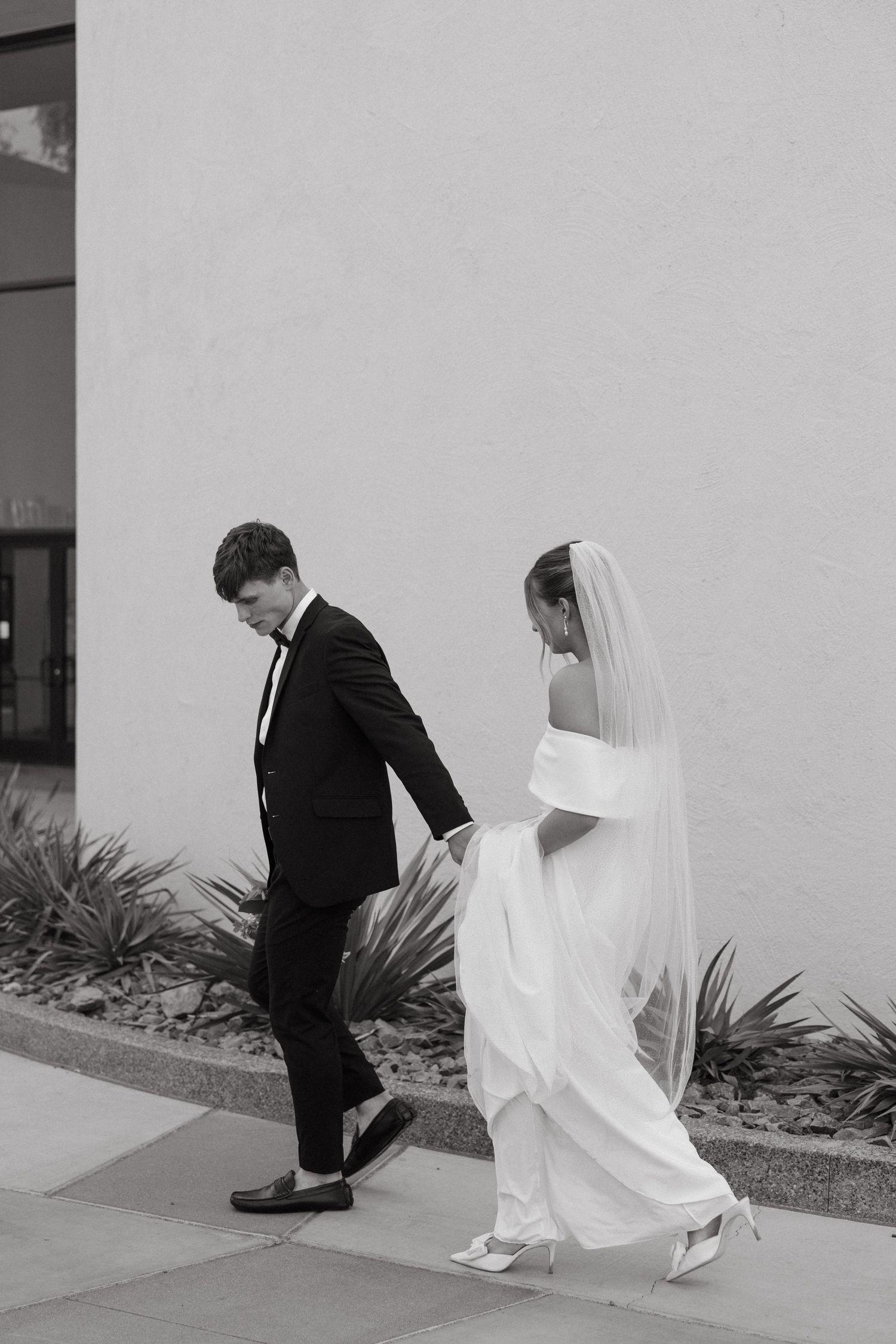 Candid black and white photo of newlyweds walking together with bride in flowing dress.