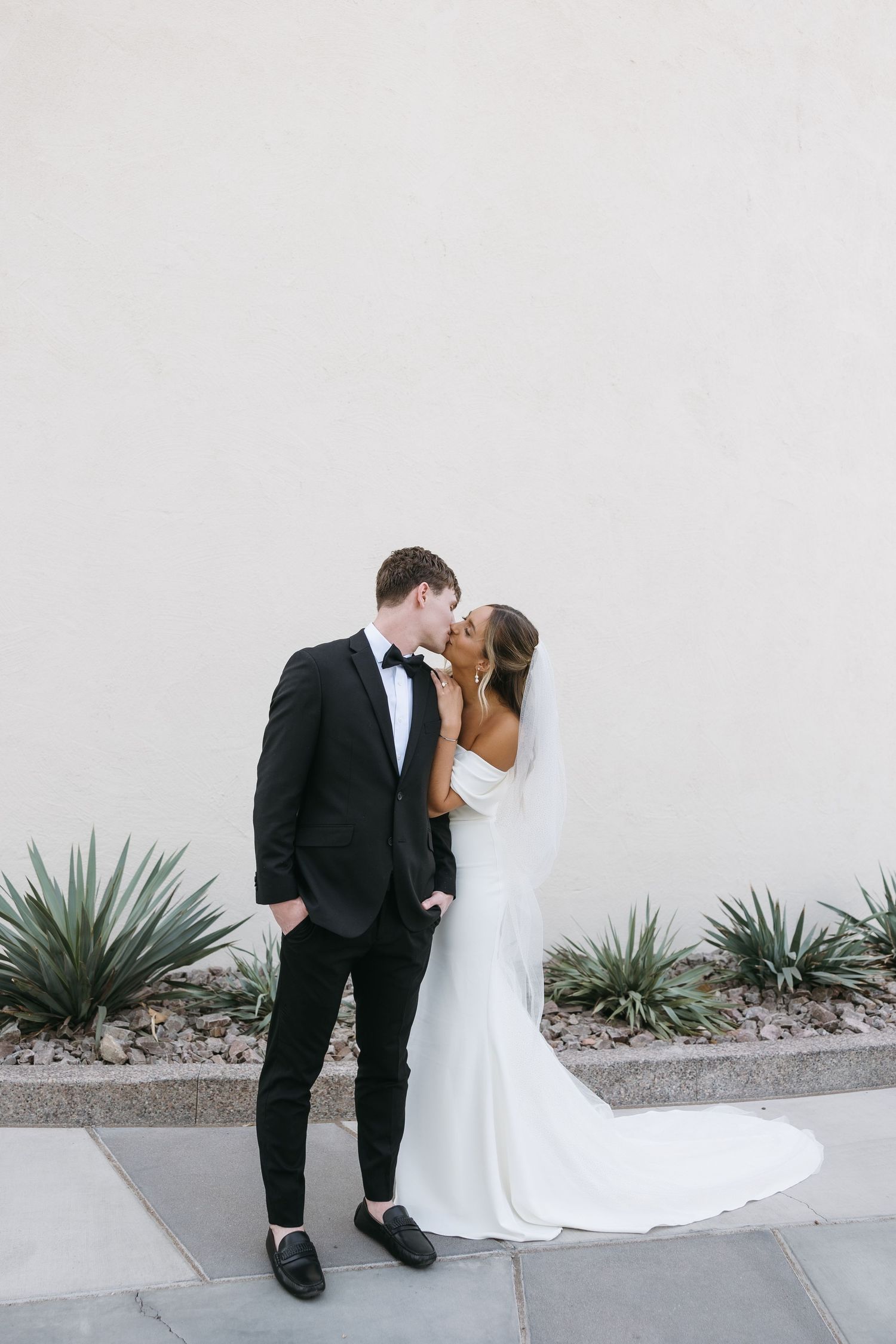 Romantic wedding portrait of couple sharing intimate moment against white wall with succulents.
