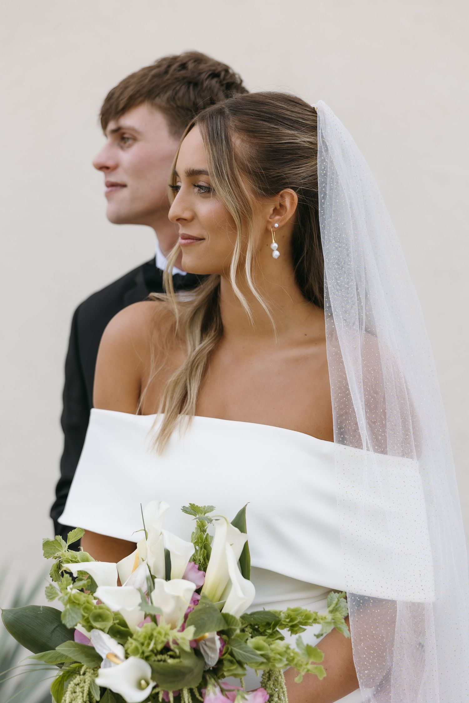 Elegant wedding portrait featuring bride in off-shoulder dress and groom in classic tuxedo.