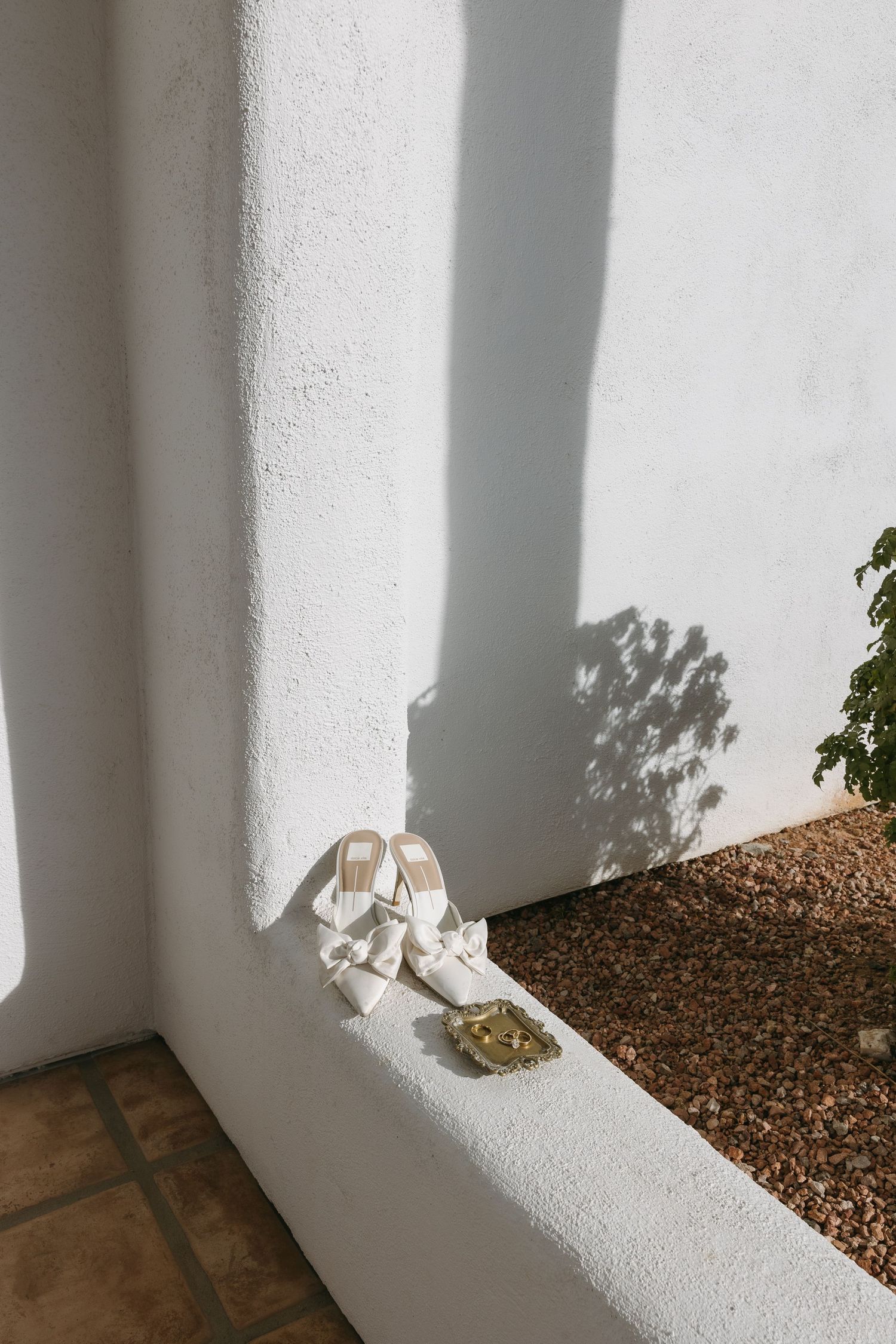 Elegant white wedding shoes placed on a textured wall ledge casting dramatic shadows.