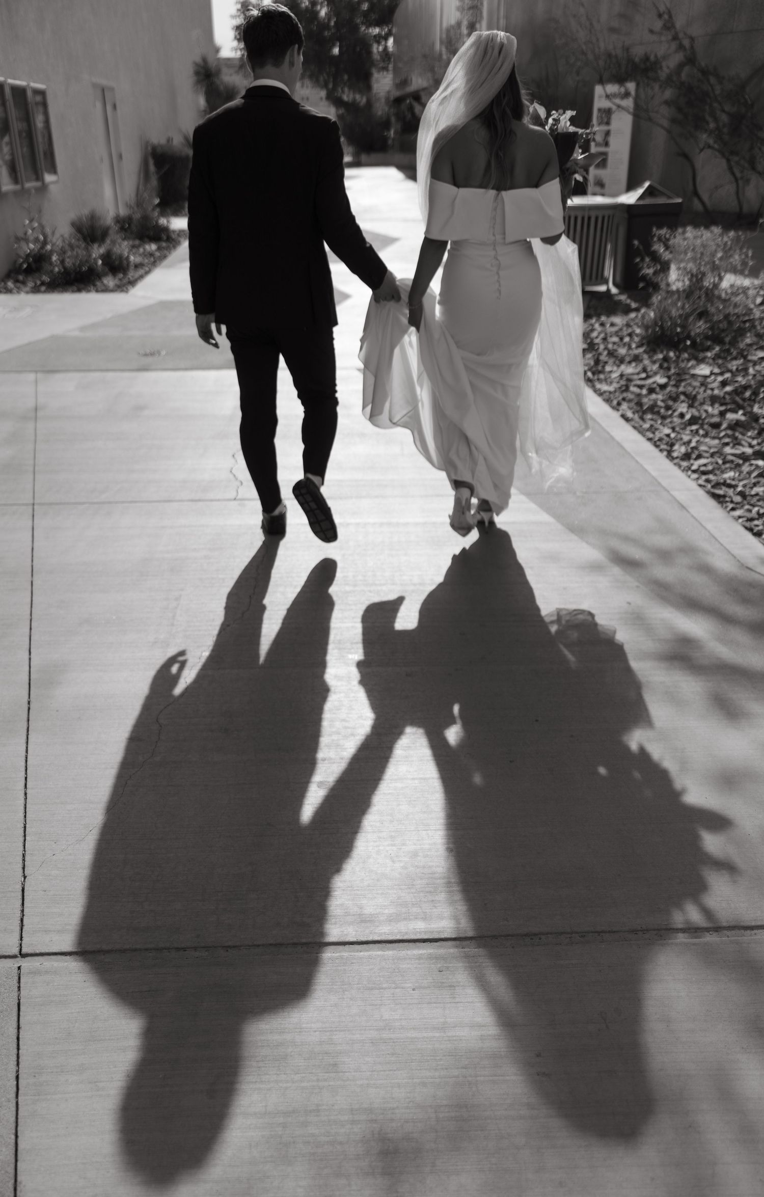 Black and white photo showing the silhouettes of a couple walking together on their wedding day.