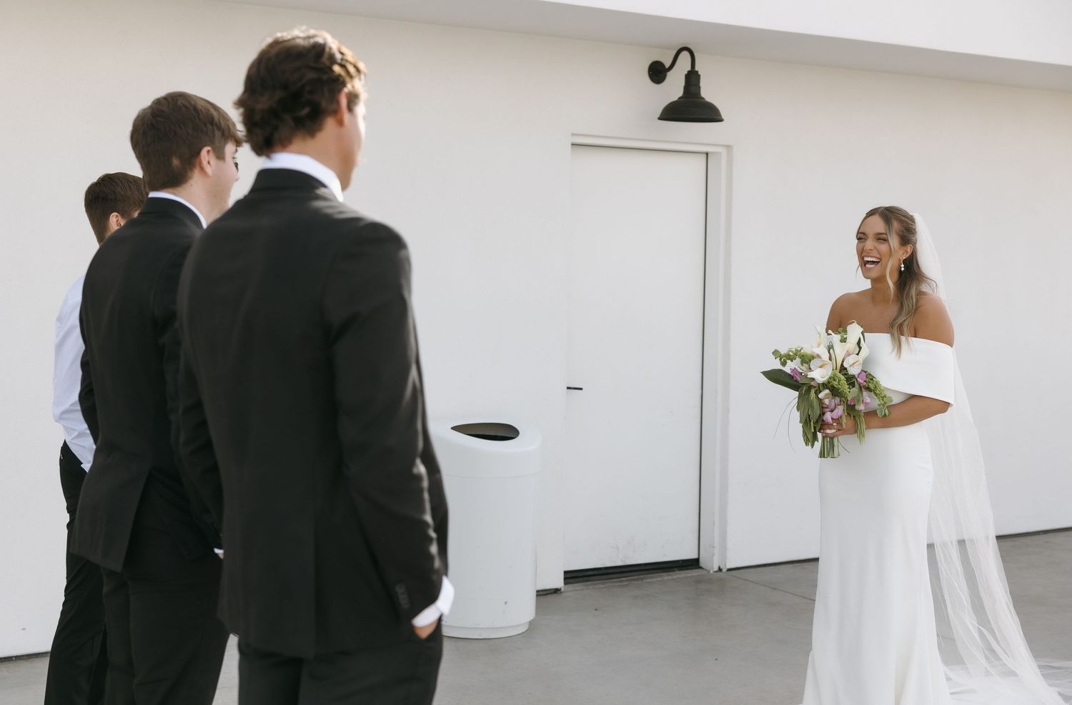 Wedding party members in black suits gather near a white door during a first look moment.