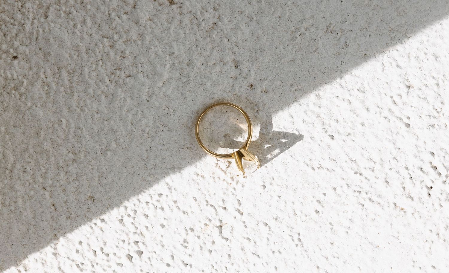 A gold wedding ring casting a shadow on a white textured surface.