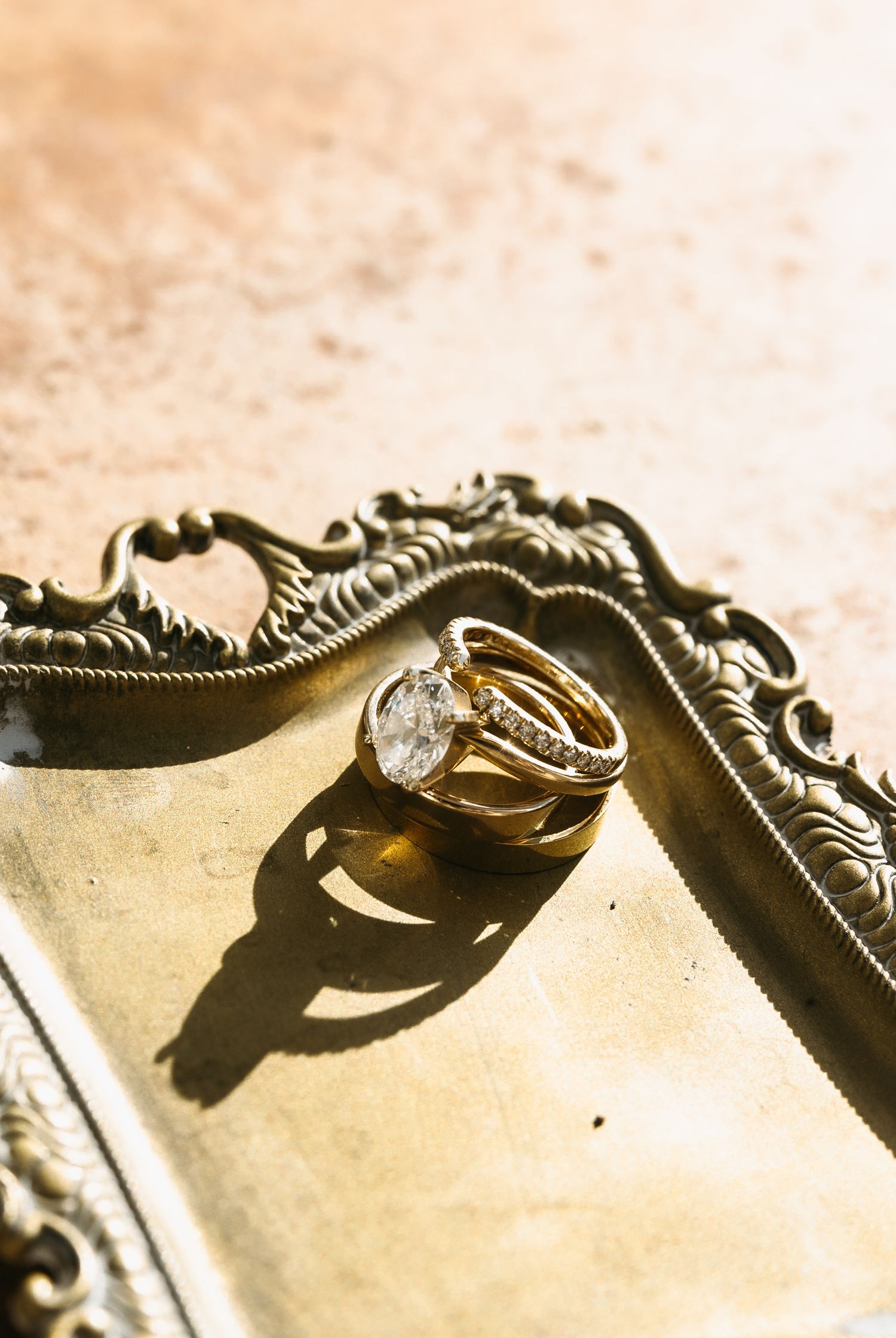 Wedding rings casting shadows on an ornate vintage mirror tray.