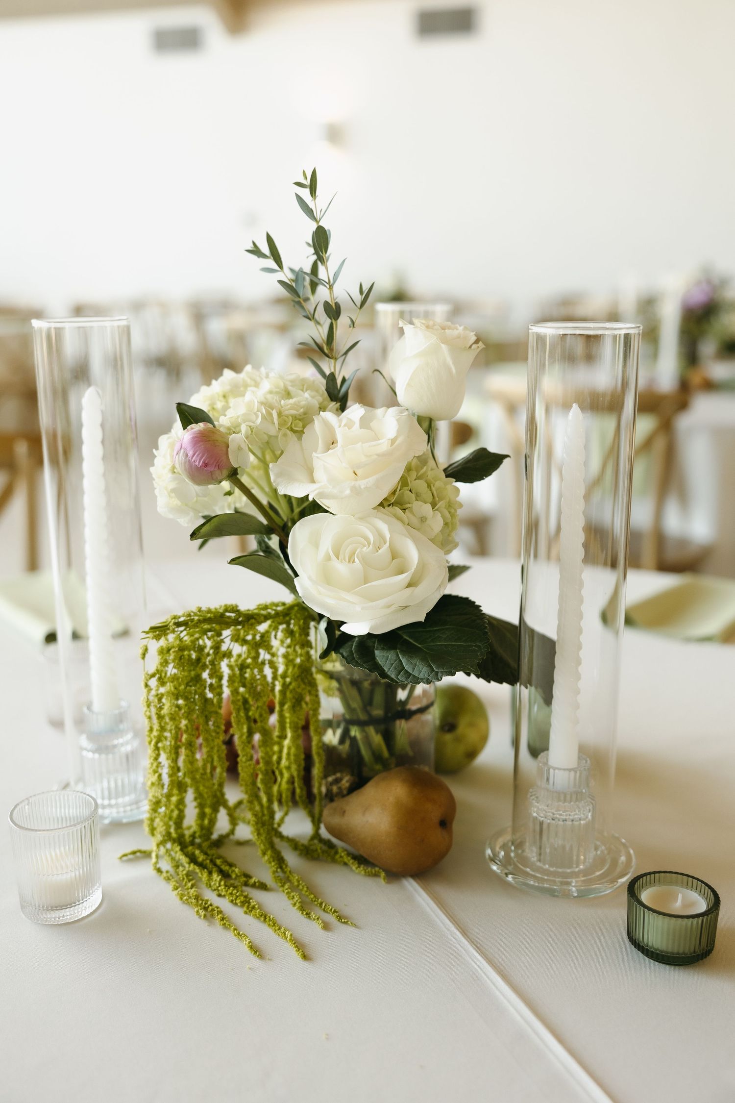 Elegant wedding centerpiece with white roses, pears, and hanging amaranthus in glass vases.
