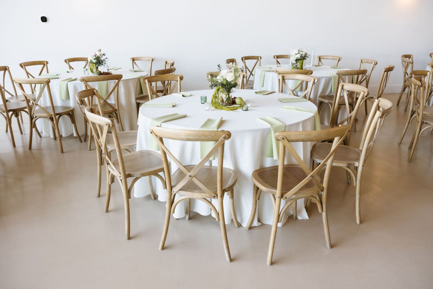 Reception hall set with round tables and rustic wooden cross-back chairs for a wedding.