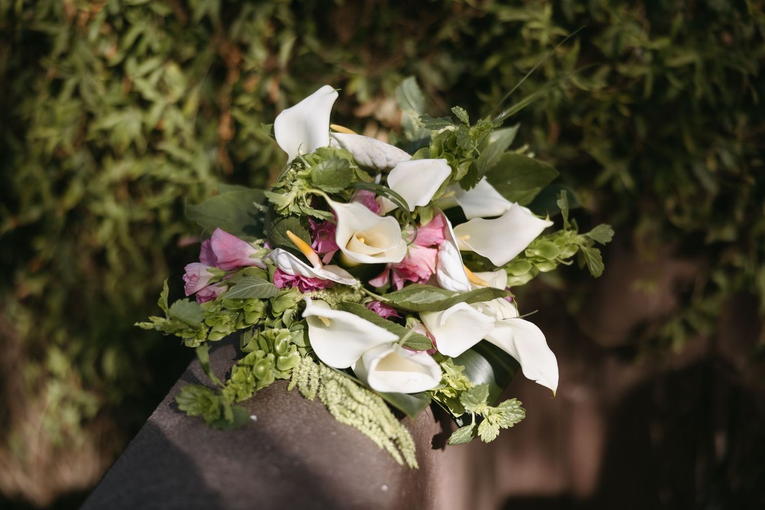 Romantic bridal bouquet with white calla lilies and pink flowers against blurred greenery.