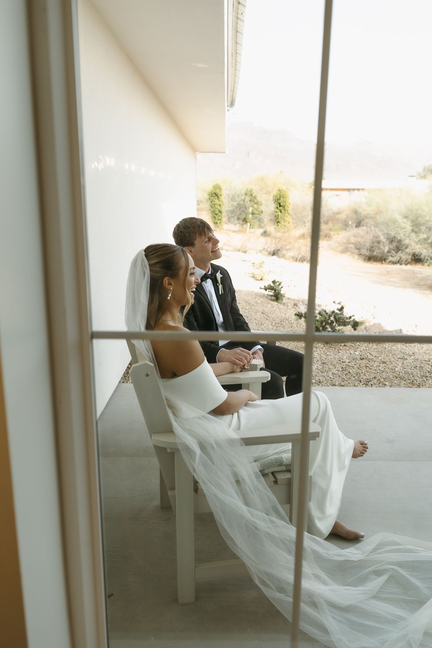 Couple sitting in white chairs on patio with desert view.